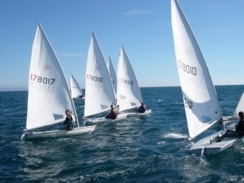 Equipo de regatas en acción en el mar abierto, navegando con velas blancas.