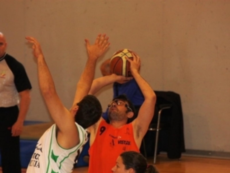 Jugador en rojo intenta anotar mientras su oponente bloquea durante un partido de baloncesto en una cancha deportiva.