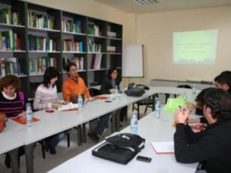 Reunión de trabajo en una biblioteca con participantes discutiendo y tomando notas.