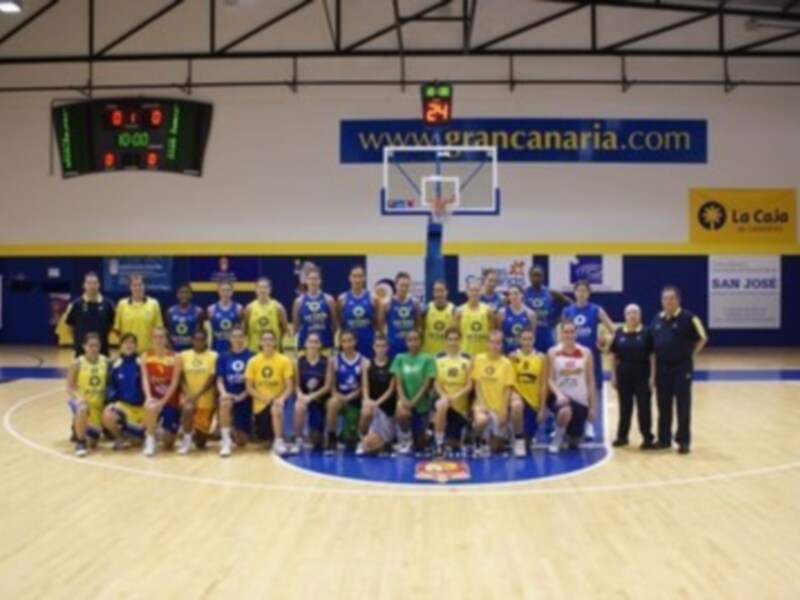 Equipo de baloncesto posando para una foto de equipo en un pabellón deportivo con el logo de Gran Canaria en el fondo.