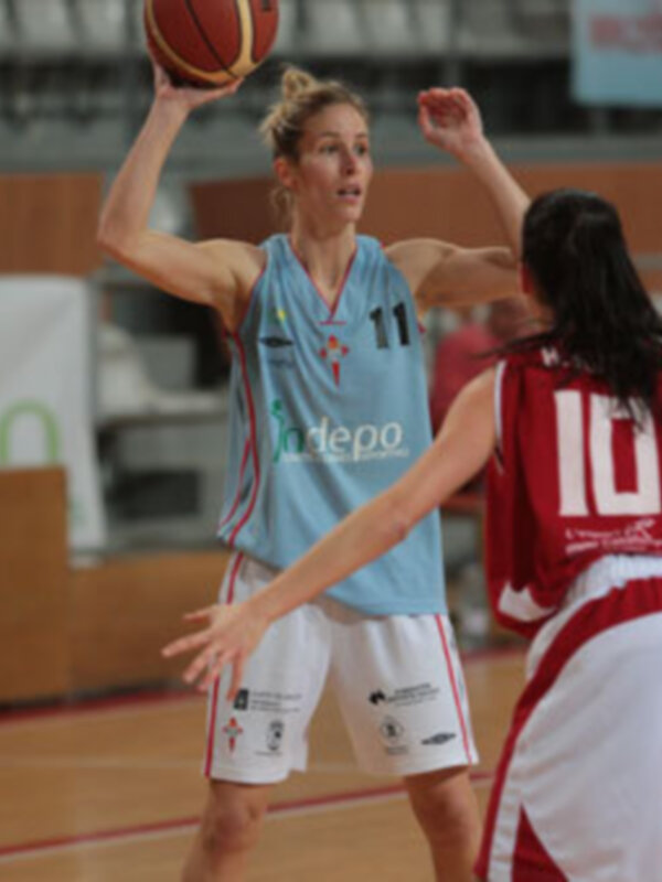 Jugadora de baloncesto en acción durante un partido, con balón en mano y oponente cerca.