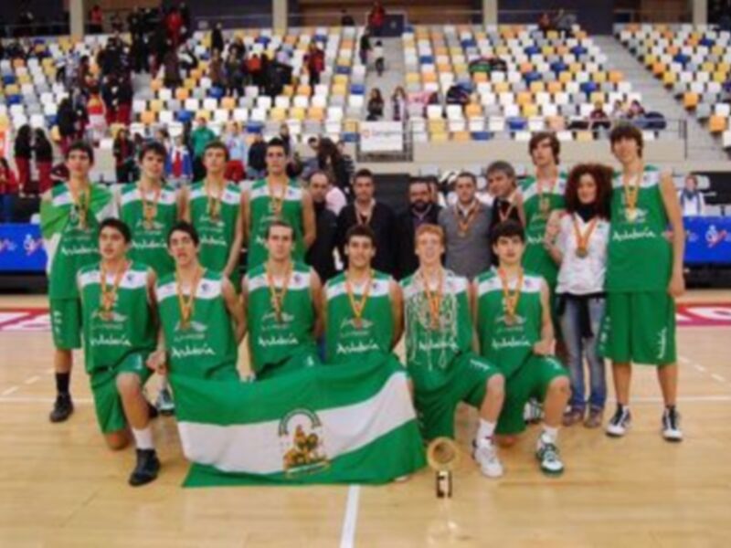 Equipo de baloncesto con medallas posando con su bandera en un pabellón deportivo.