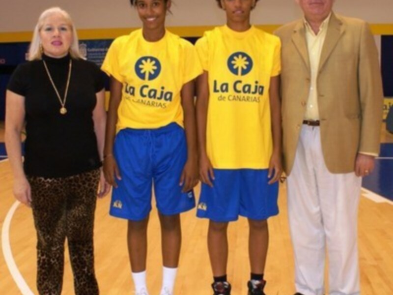 Tres personas posando en una cancha de baloncesto, dos de ellas con camisetas amarillas y azules con la inscripción 'La Caja de Canarias' y una persona adulta de pie a su lado.
