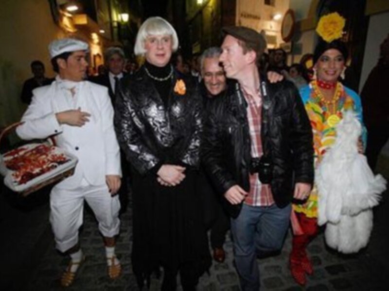 Personas vestidas con trajes tradicionales y modernos caminando por una calle adoquinada, con una atmósfera festiva y cultural.