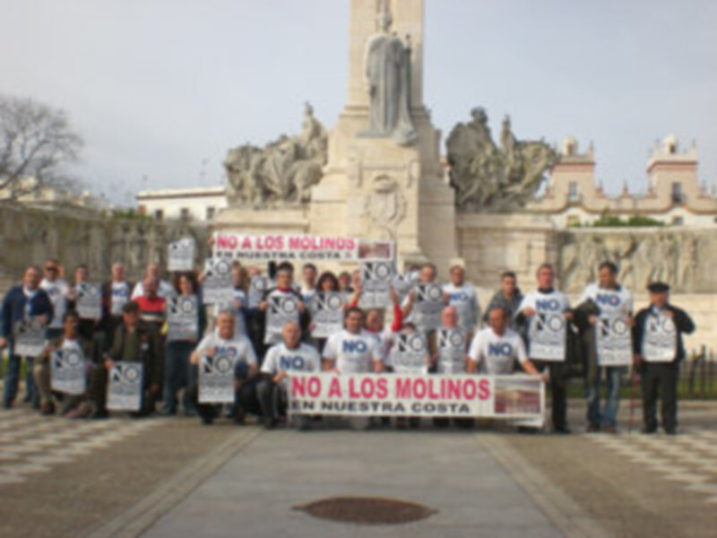 Manifestación contra los molinos eólicos en la costa, frente a una estatua monumental.