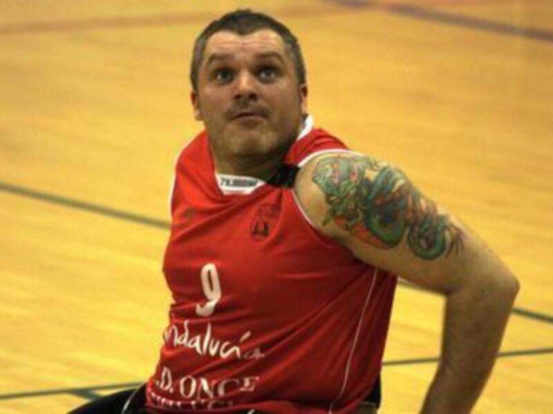 Jugador de baloncesto en silla de ruedas en acción durante un partido, mostrando su camiseta roja con el número 9 y un tatuaje en el brazo derecho.