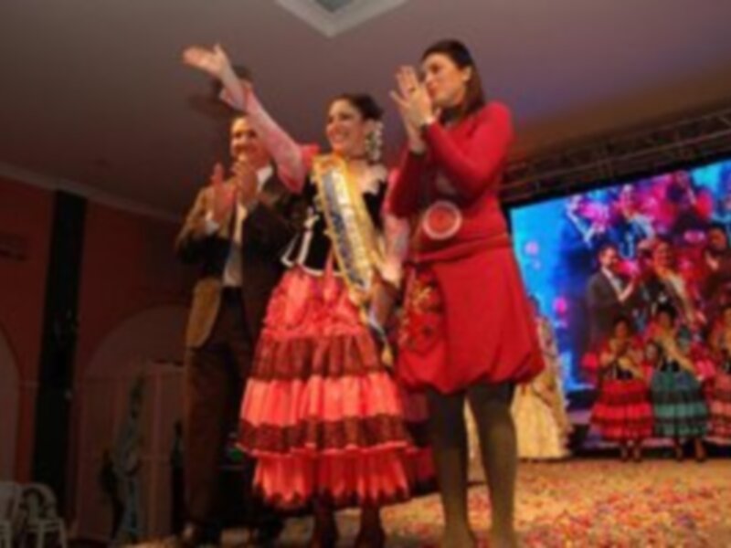 Festividad cultural con mujeres vestidas de trajes típicos y una pantalla de fondo vibrante.