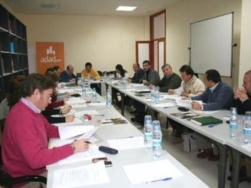 Reunión de trabajo en una sala con personas sentadas alrededor de una larga mesa con documentos y agua.