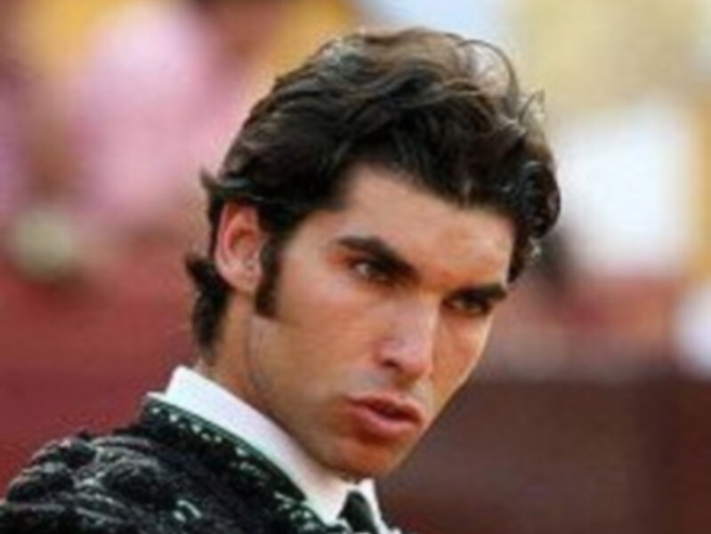 Un hombre con una camisa blanca y una corbata azul, posando para una foto en un entorno de competición deportiva.