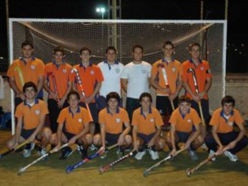 Equipo de hockey sobre césped con uniformes naranjas y blancos, posando con palos de hockey en una cancha nocturna.