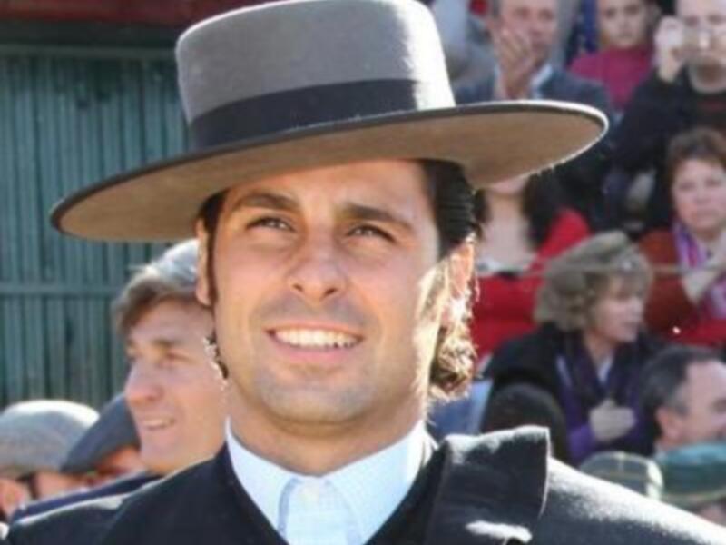 Un hombre viste traje de chaqueta y sombrero, sonriendo en un evento público.
