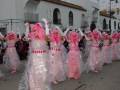 Desfile de disfraces coloridos en una calle, con participantes vestidos con trajes transparentes y accesorios brillantes.