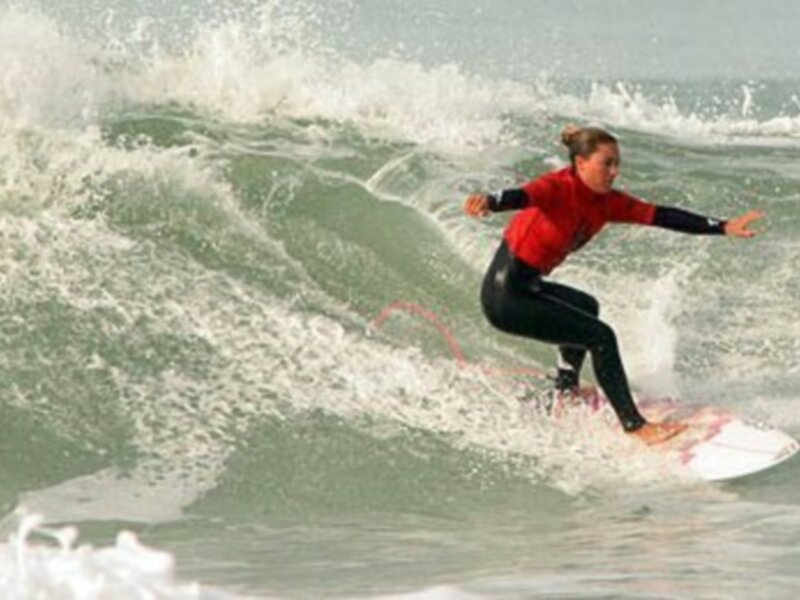 Surfista en acción, deslizándose sobre una ola en un día soleado.