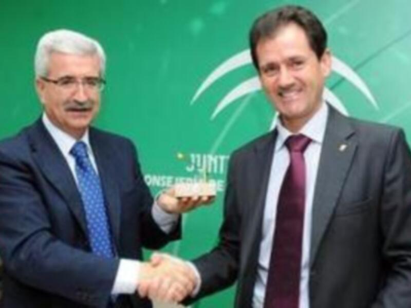 Dos hombres estrechando la mano en una reunión formal, con una bandera verde y blanca en el fondo.