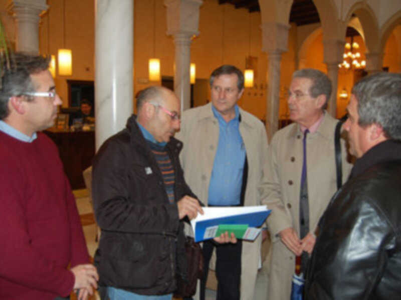 Personas intercambiando documentos en un espacio con columnas y techos altos, probablemente en un evento o reunión formal.