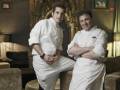 Dos chefs profesionales posan juntos en un ambiente elegante, vestidos con uniformes blancos.