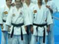 Grupo de personas vestidas con uniformes de karate, posando juntos en una tatami azul.