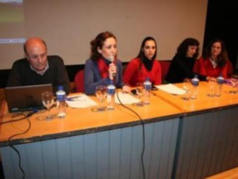 Panel de discusión en un evento académico o conferencia, con participantes sentados detrás de una mesa con microfonos y materiales de trabajo.
