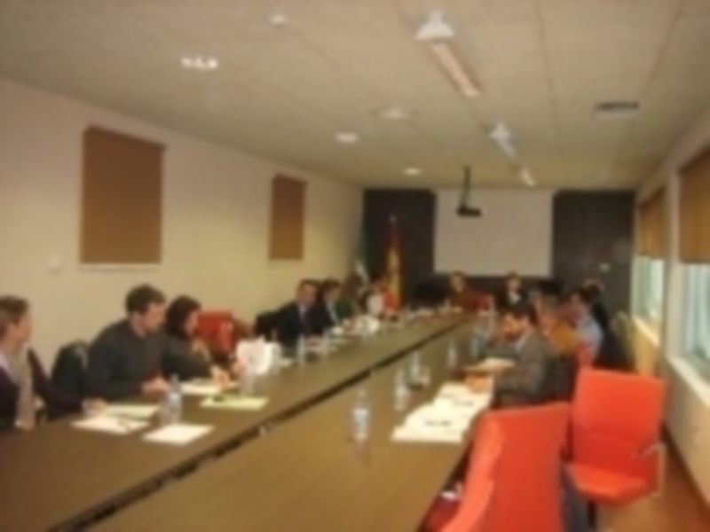 Una reunión en una sala de conferencias con personas sentadas en mesas, sosteniendo documentos y conversando.