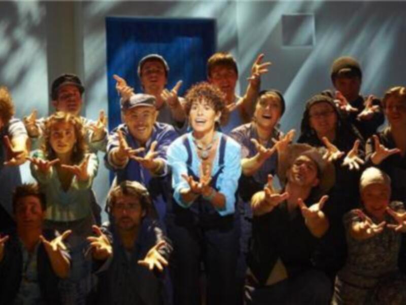 Una agrupación de personas con gestos de la mano en una escena de teatro.
