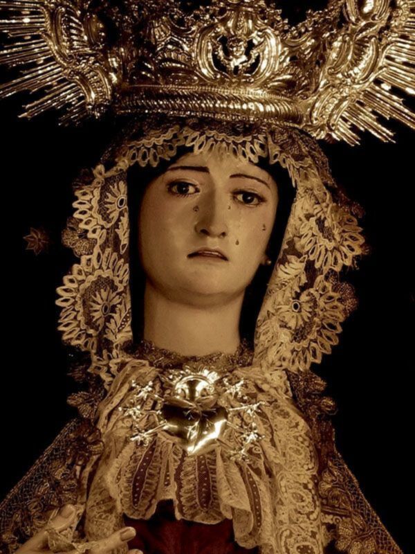 Imagen de una Virgen María con una corona dorada y un vestido ornado con detalles dorados y bordados.