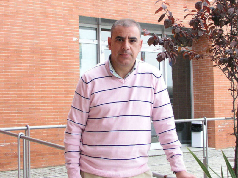 Persona en suéter rayado rosa frente a un edificio de ladrillo rojo.