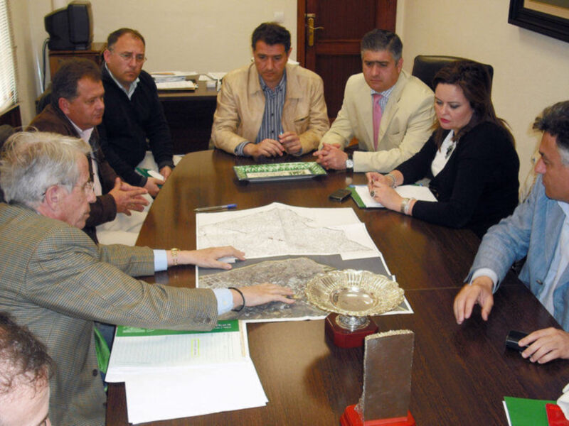 Reunión de trabajo en una oficina, personas discutiendo sobre documentos y mapas.