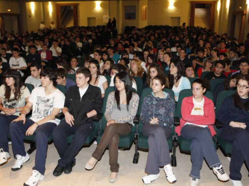 Un grupo de estudiantes sentados en una sala de conferencias, escuchando atentamente a un orador.
