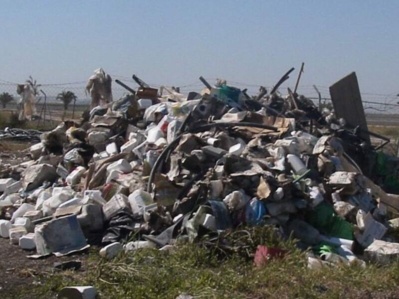 Pila de basura en un área rural, con contenedores y plásticos desechados.