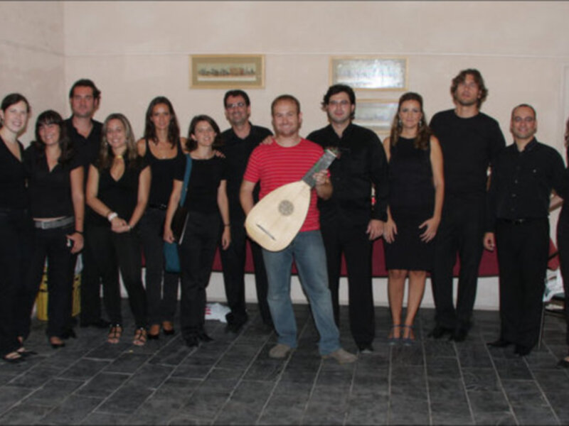 Grupo de personas posando con un músico sosteniendo un lute en un salón decorado con cuadros.