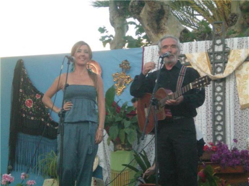 Una mujer y un hombre están en una escena musical al aire libre, con la mujer vestida de azul y el hombre tocando un violín.