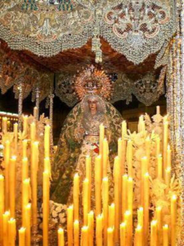 Virgen de la Esperanza en su trono ornado con candelabros y velas iluminando el ambiente.