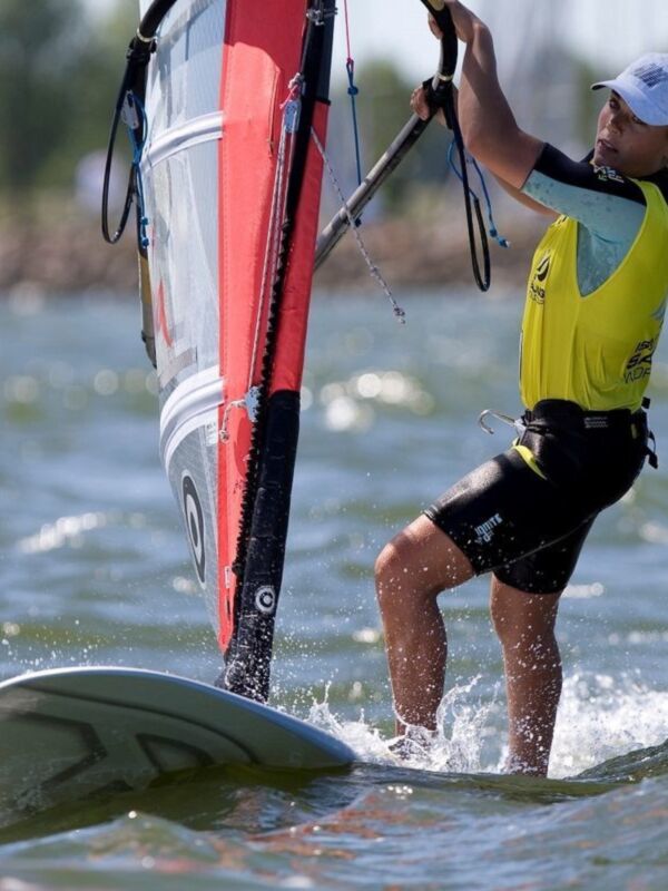 Una persona practicando windsurf en el agua, con un casco de seguridad y un surf de color rojo y blanco.