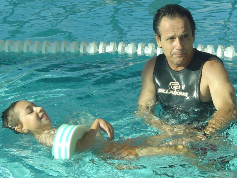 Adulto enseñando a nadar a un niño en una piscina con un flotador.