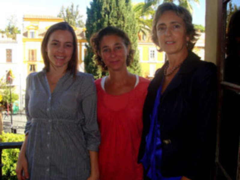 Tres personas sonrientes en una calle con edificios y árboles al fondo.