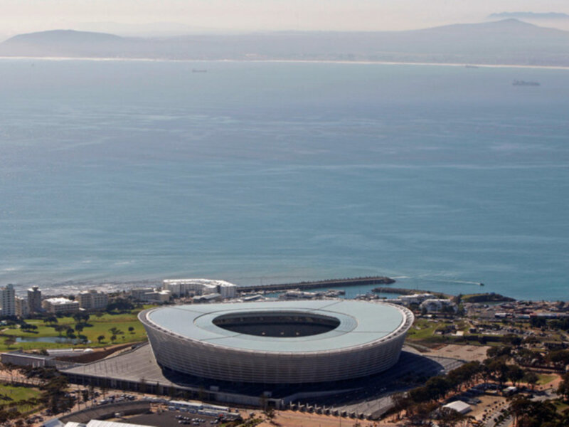 Estadio de fútbol moderno con vista al mar y montañas en el fondo.