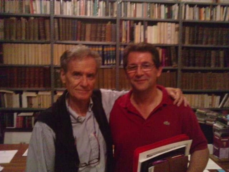 Dos hombres sonrientes en una biblioteca llena de libros.