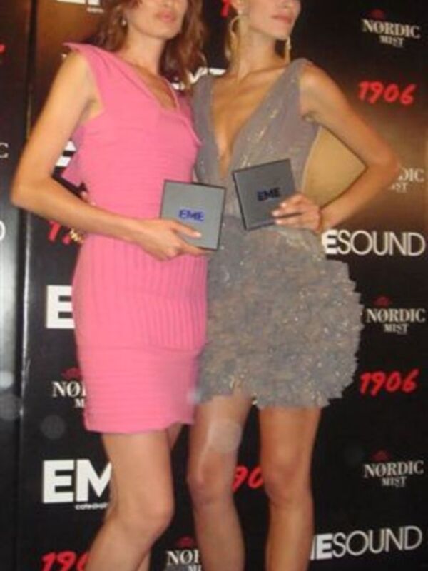 Dos mujeres posan con vestidos de color rosa y gris en un evento con el logotipo de 'Nordic Sound' en el fondo.