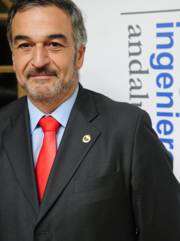 Hombre con traje y corbata roja, sonriendo en un evento profesional.