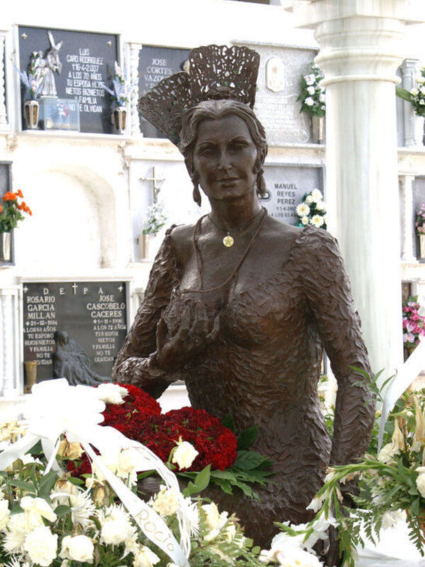 Estatua de bronce de una mujer con flores en un cementerio.