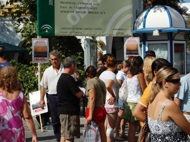 Un grupo de personas caminando por una calle, con un cartel informativo en el fondo.