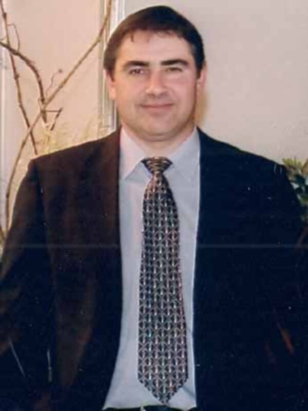 Retrato de hombre en traje y corbata, fondo neutro con ramas de planta en el lateral.