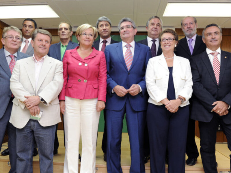 Grupo de personas en trajes y chaquetas posando juntos en una sala formal.