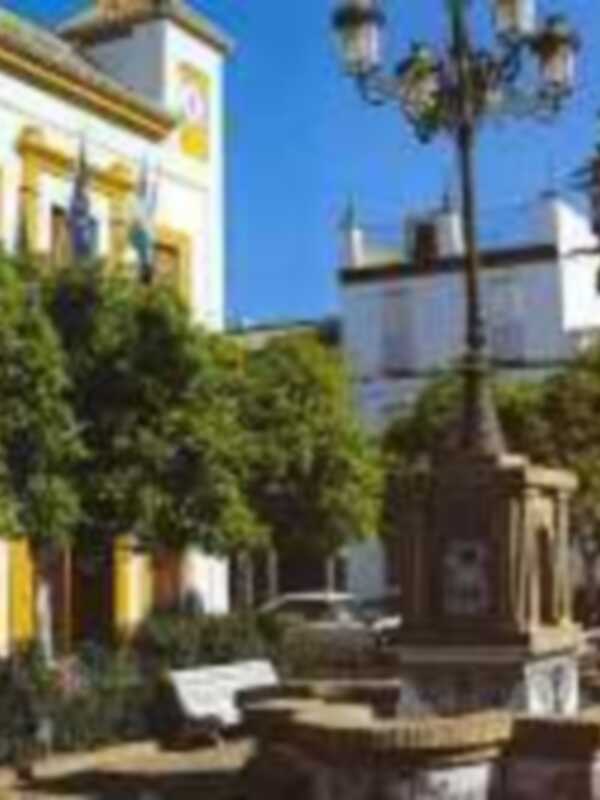 Plaza con fuente y farola histórica en un entorno urbano con edificios amarillos y verdes.