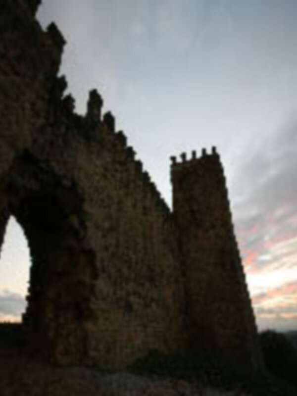 Ruinas de un castillo medieval en un paisaje de crepúsculo, con un cielo nublado y una torre de defensa en primer plano.
