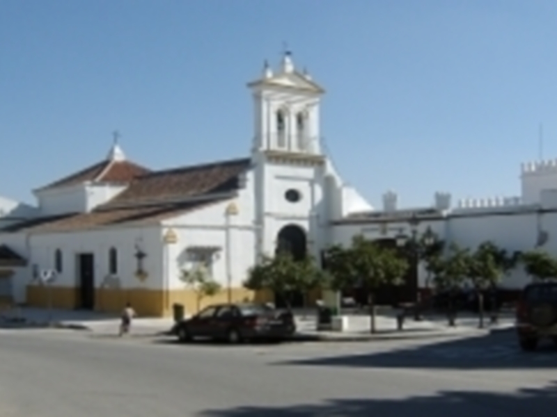 Iglesia histórica con torre blanca y tejados rojos en un paisaje urbano soleado.