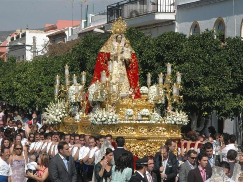 Procesión religiosa con estandarte de Virgen María, rodeada por una multitud en una calle urbana.
