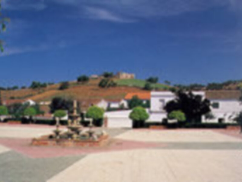 Plaza tranquila con fuente y edificios blancos en un paisaje montañoso.