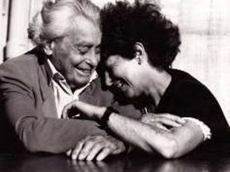 Dos personas conversando en una mesa, uno de ellos con una camisa blanca y el otro con una camisa negra.