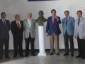 Grupo de hombres en trajes posando frente a una estatua o busto.